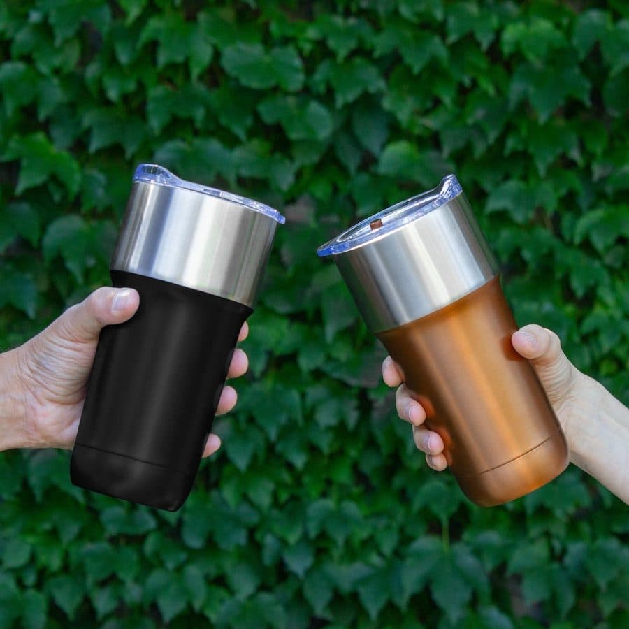 Dos vasos térmicos de acero, uno negro y uno cobre, sostenidos frente a un muro de hiedra