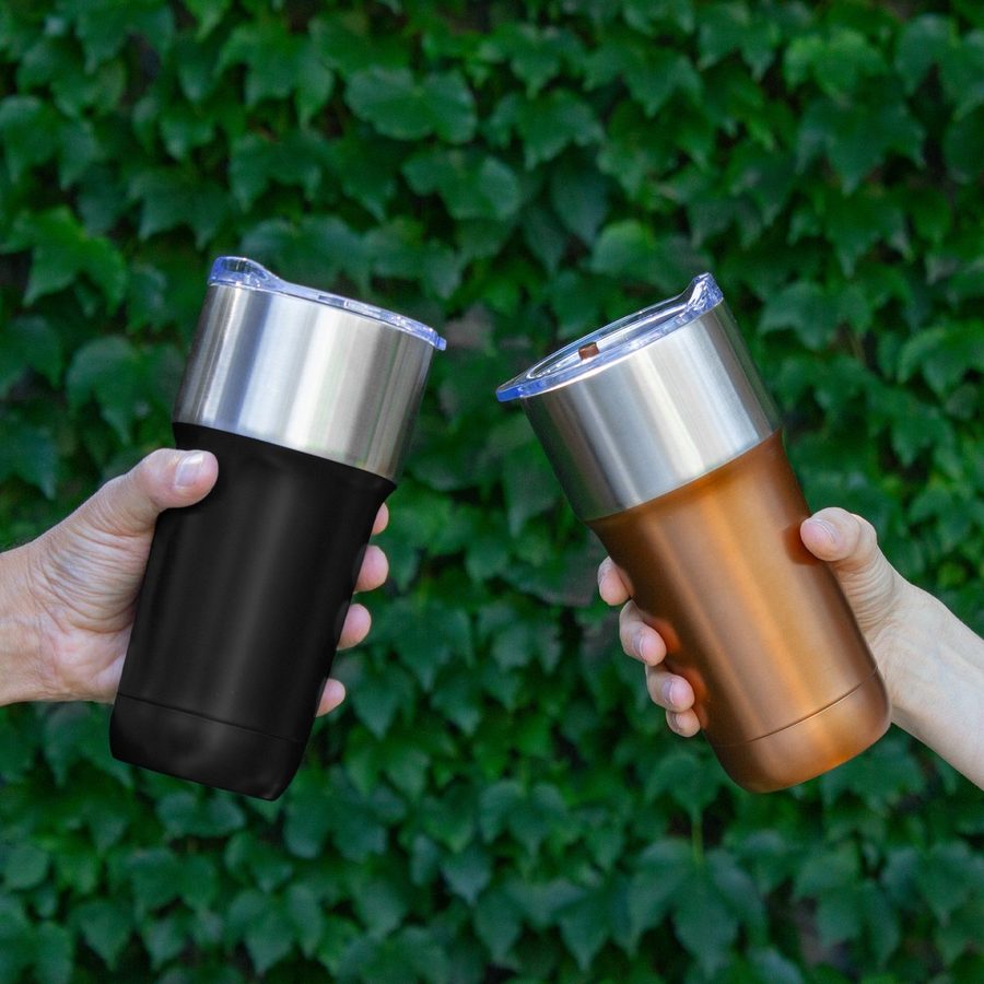 Dos vasos térmicos de acero, uno negro y uno cobre, sostenidos frente a un muro de hiedra